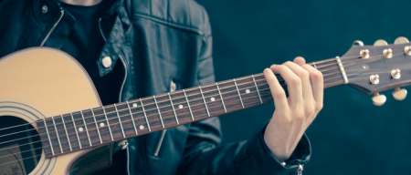 person wearing a dark jacket pressing some frets for a chord on an acoustic guitar